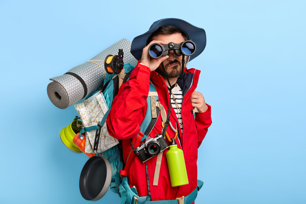 serious-unshaven-male-backpacker-keeps-binoculars-near-eyes-wears-hat-red-jacket-explores-new-way-carries-tourist-backpack (1)